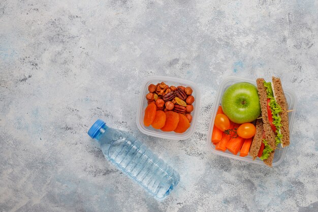 Lunchbox z kanapką, warzywami, owocami na bielu.