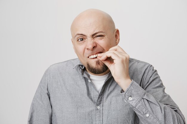 Łysy brodaty mężczyzna w średnim wieku dotyka zębów