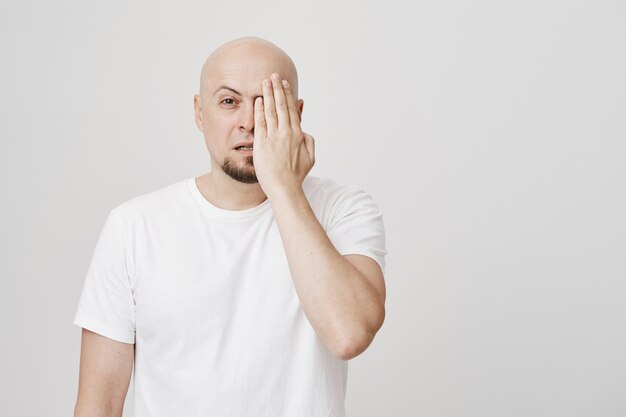 Łysy mężczyzna w średnim wieku zasłania jedno oko, sprawdzając wzrok u optyka