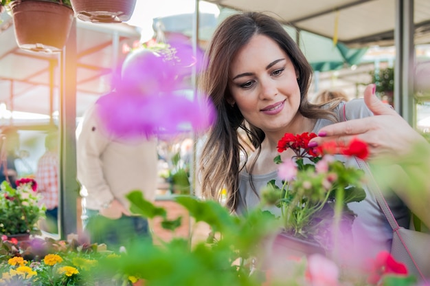 M? Oda kobieta gospodarstwa geranium w gliniane doniczki w centrum ogrodu. Młoda kobieta zakupy kwiaty na centrum ogrodu centrum