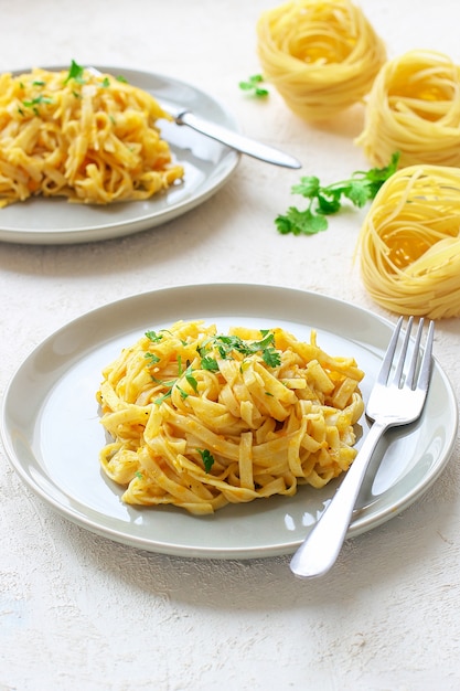 Makaron fettucine z dyni i alfredo w ceramicznym talerzu ze świeżymi, surowymi plasterkami dyni piżmowej. Jesienny posiłek na lunch. Przepis na squash Butternut.