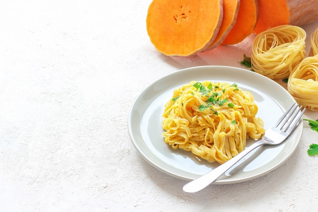 Makaron fettucine z dyni i alfredo w ceramicznym talerzu ze świeżymi, surowymi plasterkami dyni piżmowej. Jesienny posiłek na lunch. Przepis na squash Butternut.