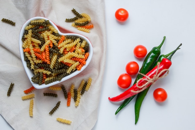 Bezpłatne zdjęcie makaron fusilli w misce z papryką, pomidorami płasko leżał na stole białym i obrusowym