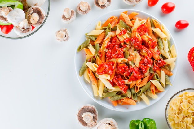 Makaron penne w talerzu z surowym makaronem, pieczarkami, pomidorem, pieprzem, sosem