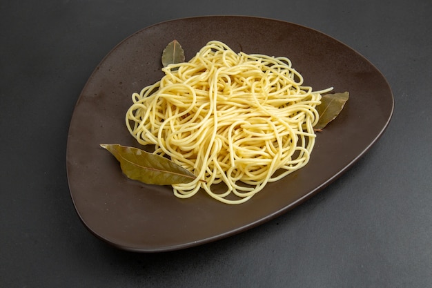 Makaron spaghetti z widokiem z dołu z liśćmi laurowymi na półmisku na czarnym tle