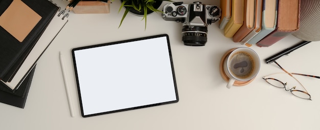 Makieta tabletu na białym stole roboczym z filiżanką kawy, szklankami, notatnikami, aparatem do książek i doniczką