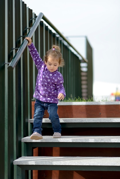 Mała 20-miesięczna dziewczynka schodzi po schodach na zewnątrz