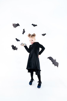Mała czarownica dziewczyna w czarnej długiej sukni i magicznych akcesoriach. halloween