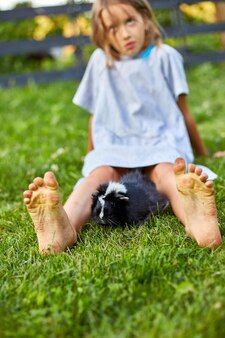 Mała dziewczynka bawi się czarną świnką morską siedzącą na zewnątrz latem, świnka morska perkal pasie się na trawie na podwórku właściciela, kochają zwierzęta