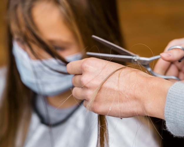 Mała dziewczynka dostaje fryzurę podczas noszenia maski medycznej