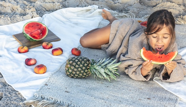 Mała dziewczynka je owoce leżąc na kocu na plaży