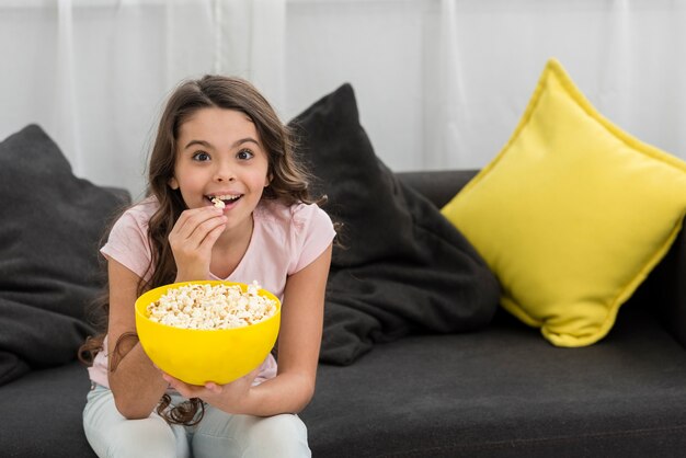 Mała dziewczynka jedzenie popcornu na kanapie