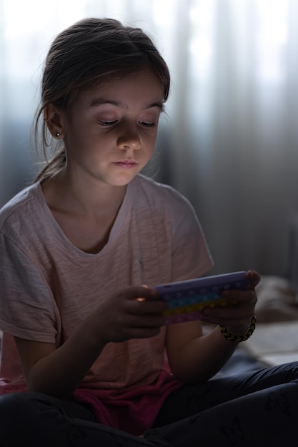 Bezpłatne zdjęcie mała dziewczynka korzysta z telefonu, siedząc wieczorem w łóżku