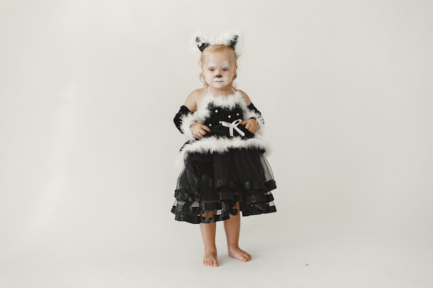 Mała dziewczynka maluch ubrana w czarną sukienkę jak kot. Dziewczyna ma twarz pomalowaną jak twarz kota