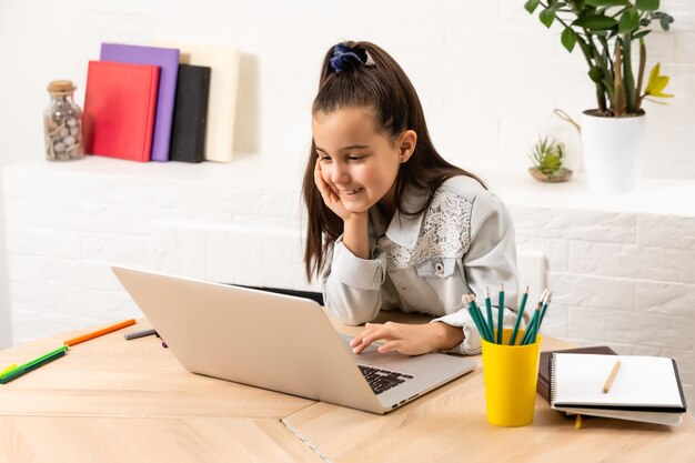 Mała dziewczynka odrabia pracę domową w domu i korzysta z laptopa