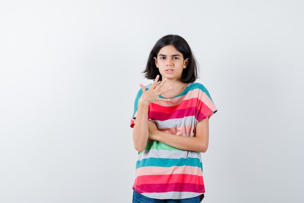 Mała dziewczynka podnosząc rękę, wzruszając ramionami w t-shirt i patrząc na zdziwionego, widok z przodu.