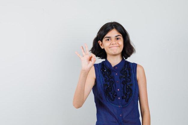 Mała dziewczynka pokazuje ok gest w niebieskiej bluzce i wygląda na zadowoloną.