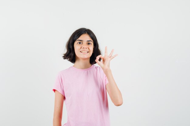 Mała dziewczynka pokazuje ok gest w różowej koszulce i wygląda jowialnie. przedni widok.