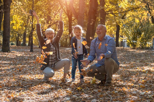 Mała dziewczynka rzuca liście w parku z dziadkami jesienią