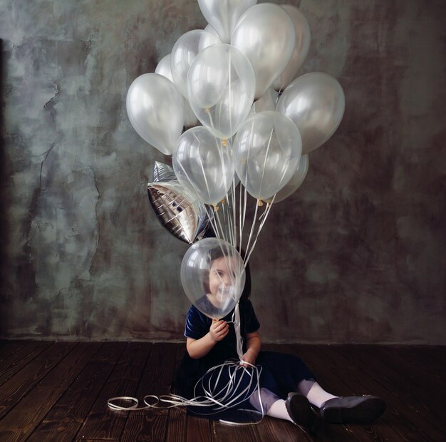 Mała dziewczynka siedzi na podłodze i trzyma balony w pokoju