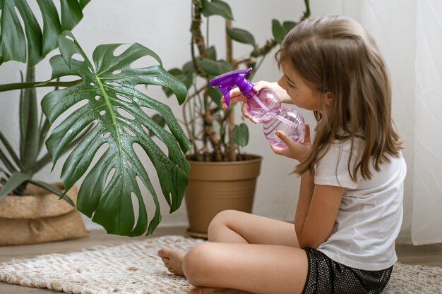 Mała dziewczynka spryskuje liście rośliny doniczkowej, opiekując się rośliną Monstera.