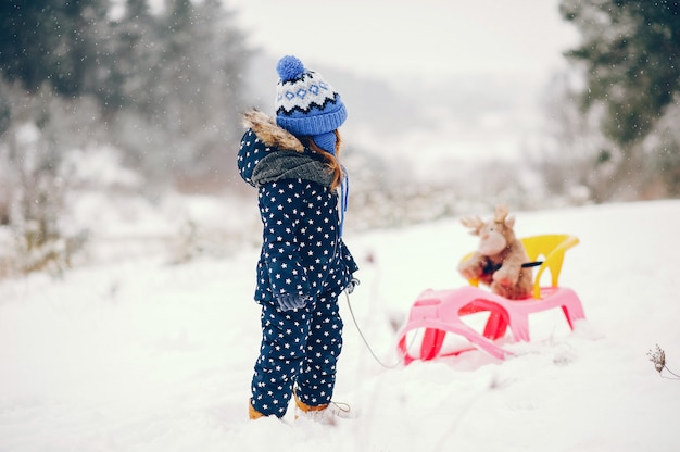 Mała dziewczynka w błękitnym kapeluszu bawić się w zima lesie