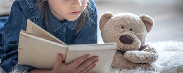 Bezpłatne zdjęcie mała dziewczynka w domu, leży na podłodze ze swoją ulubioną zabawką i czyta książkę.
