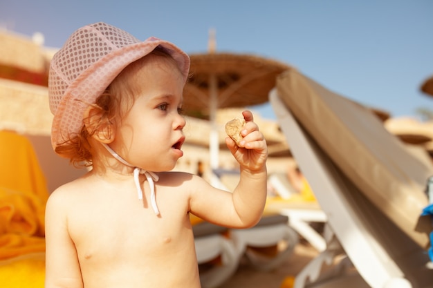 Mała dziewczynka w panamie bawić się z kamykiem na plaży pod ochroną parasoli