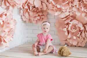 Bezpłatne zdjęcie mała dziewczynka w różowej sukience siedzi wśród dużych różowe kwiaty papieru