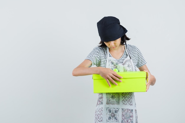 Mała dziewczynka w sukni kuchennej patrząc na obecne pudełko i wyglądająca na zaciekawioną