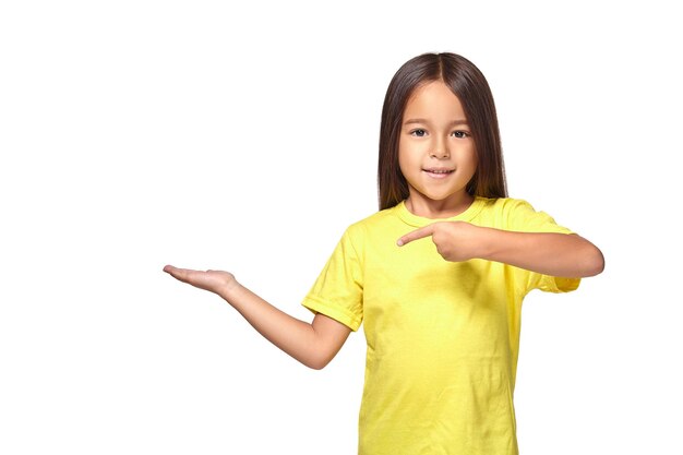 Mała dziewczynka w żółtej koszulce wyciąga rękę i pokazuje miejsce na kopię dla twojego produktu na białym tle