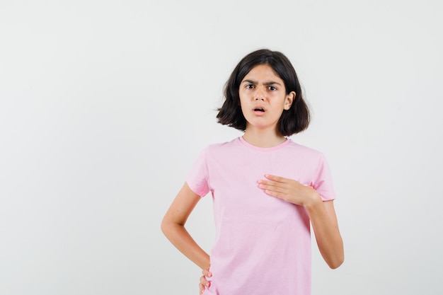 Mała dziewczynka wskazuje na siebie w różowej koszulce i wygląda na zdziwioną. przedni widok.