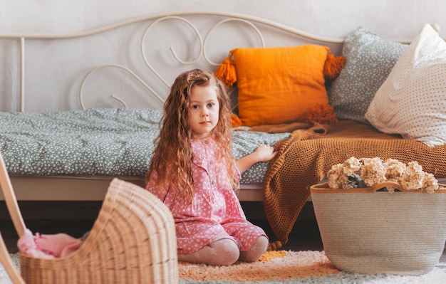 Mała dziewczynka z kręconymi włosami bawi się na podłodze w dziecięcej sypialni. szczęśliwe dzieciństwo