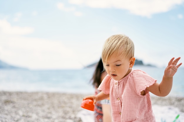 Mała dziewczynka z pleśnią w dłoni stoi na kamienistej plaży ze spuszczonymi oczami