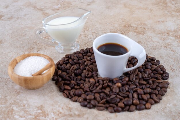 Mała miska cukru obok stosu ziaren kawy otaczających filiżankę kawy