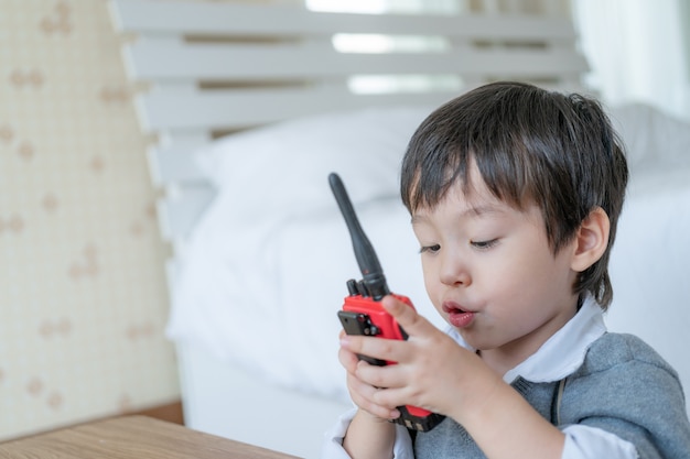 Mała śliczna chłopiec cieszy się opowiadać z czerwonym walkie-talkie redio w sypialni