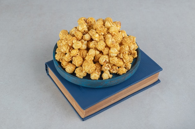 Bezpłatne zdjęcie mała tacka z popcornem pokrytym karmelem umieszczona na marmurowej książce.
