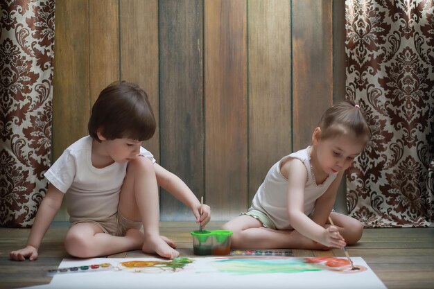Małe dzieci malują na dużej kartce papieru na podłodze