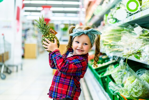 Małe dziecko stoi z ananasem w supermarkecie