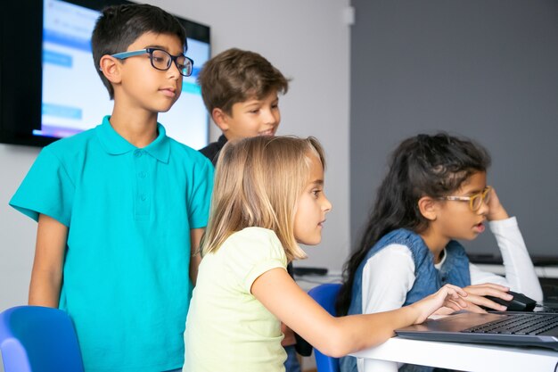 Małe dziewczynki korzystające z laptopów, uczące się w szkole komputerowej i siedzące przy stole