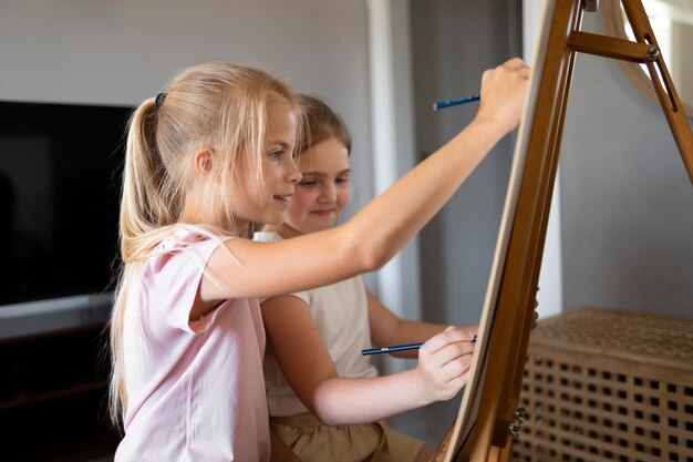 Małe dziewczynki wspólnie rysują sztalugami w domu