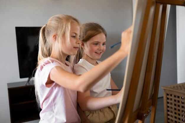 Małe dziewczynki wspólnie rysują sztalugami w domu