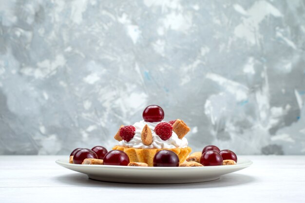 małe kremowe ciasto z malinami i ciasteczkami na biało-jasnym biurku, tort owocowy słodko-jagodowy krem wiśniowy
