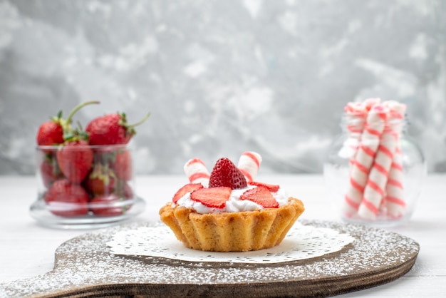 Bezpłatne zdjęcie małe pyszne ciasto ze śmietaną i pokrojonymi truskawkami różowe cukierki na białym, ciasto jagodowe słodkie pieczone pieczone owoce