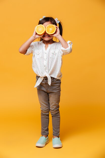 Małej dziewczynki dziecko zakrywa oczy z pomarańcze.