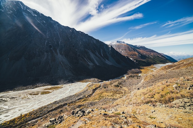 Malowniczy górski krajobraz z górską rzeką i jeziorem w dolinie wśród wysokich gór ze śniegiem w jesiennych kolorach w słońcu. niesamowity alpejski widok na pstrokatą dolinę górską pod chmurami cirrus.