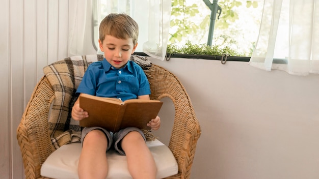Bezpłatne zdjęcie mały chłopiec czyta książkę siedząc na fotelu w przyczepie kempingowej