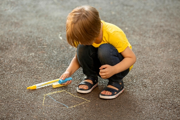Bezpłatne zdjęcie mały chłopiec w parku, rysowanie kredą