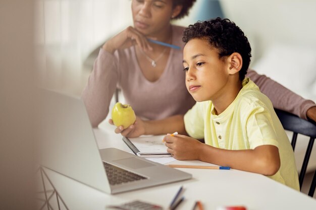 Mały czarny chłopiec używający laptopa podczas nauki w domu z matką