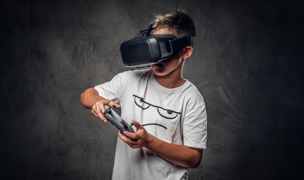 Mały, modny dzieciak gra w nową grę wideo za pomocą specjalnych gogli wirtualnej rzeczywistości i joysticka.